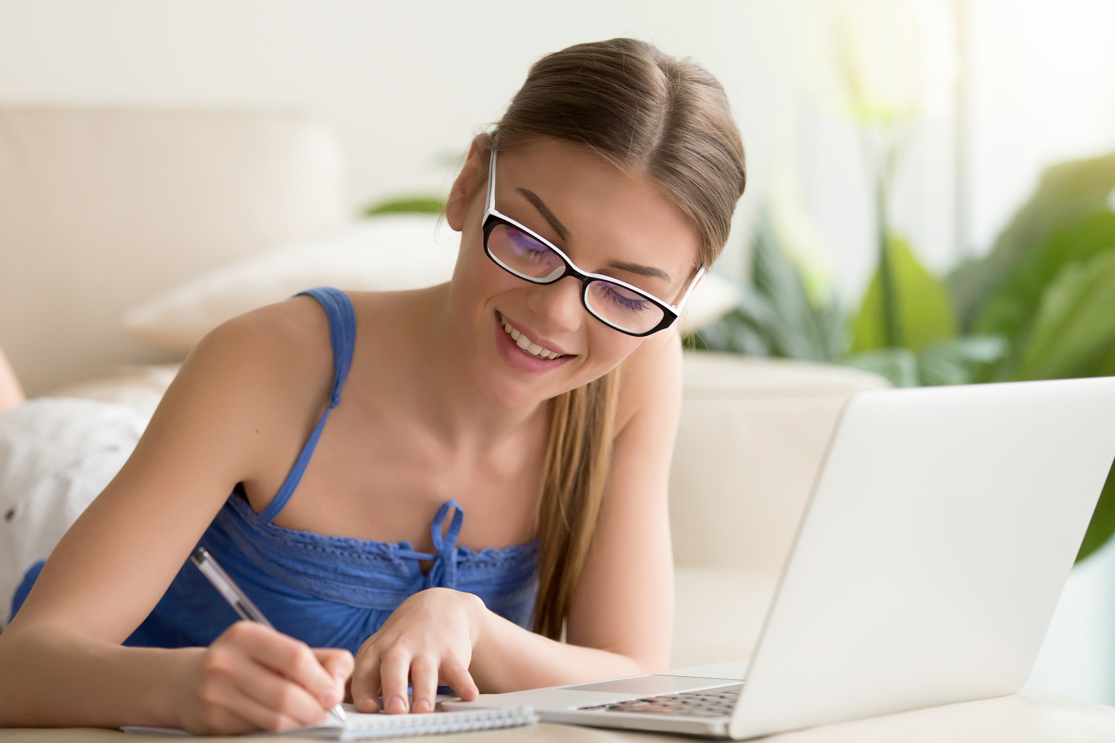 woman smiling as she writes in her notebook next to a laptop