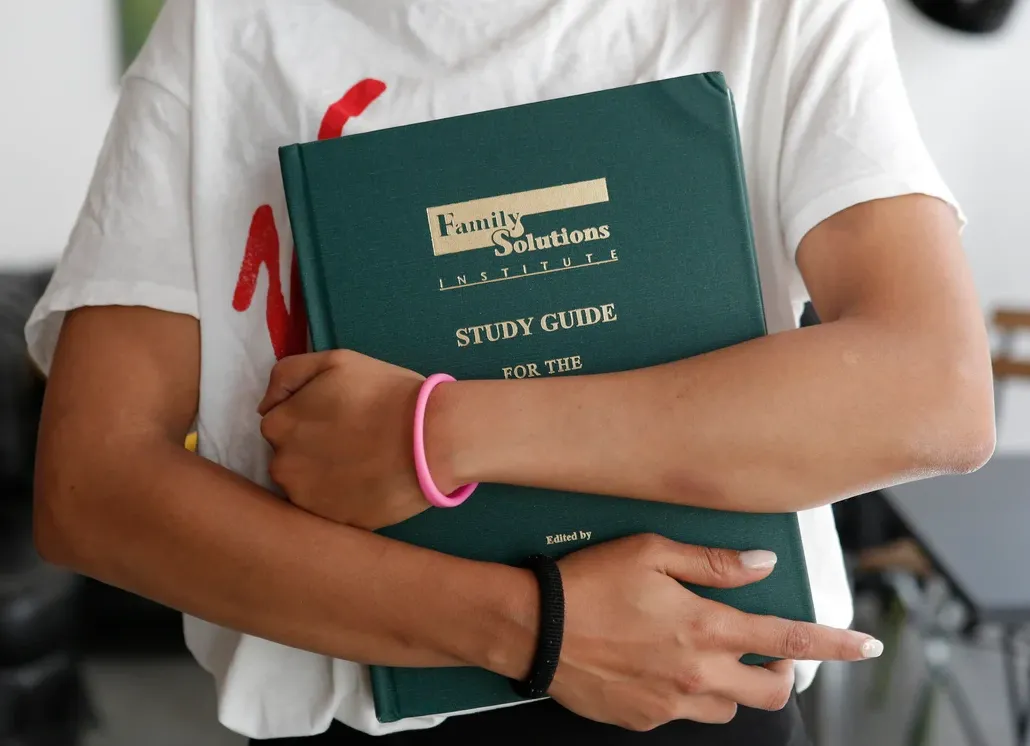 Study Guide Family Solutions Institute big green book in the arms of a student