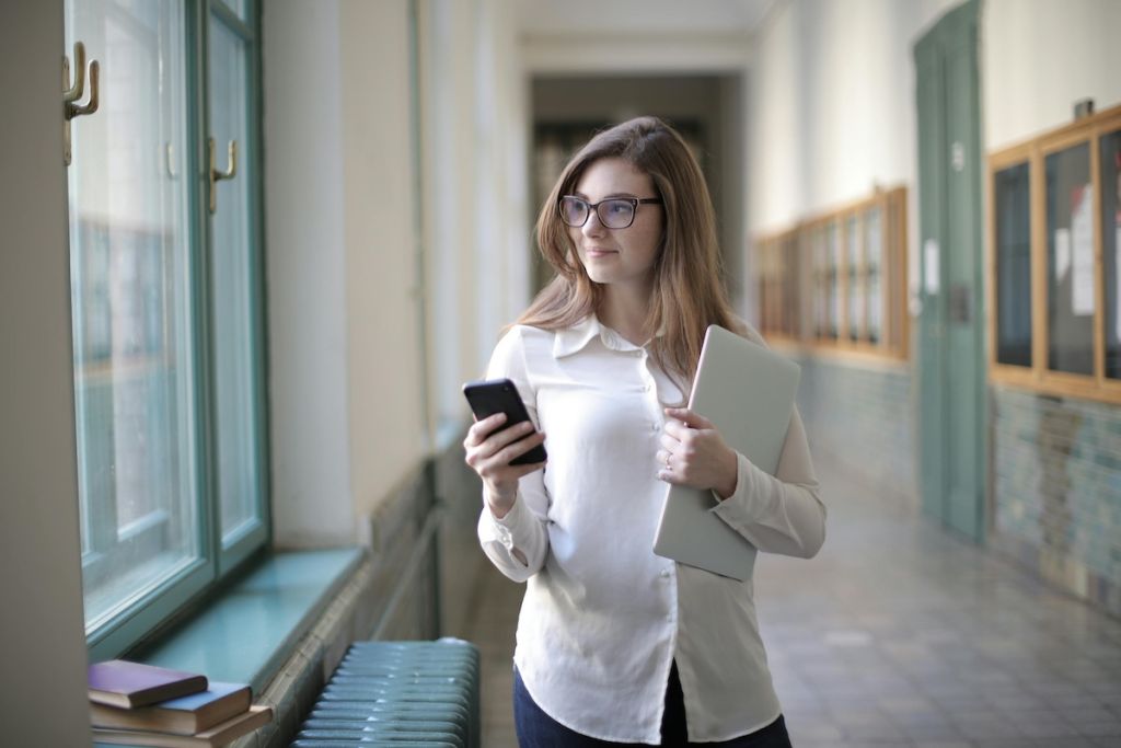 confident woman walking down hallway with phone and notebook
